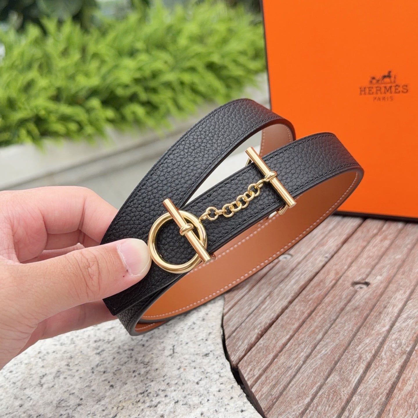 Handheld black leather belt with tan edge, gold buckle, linked chain
