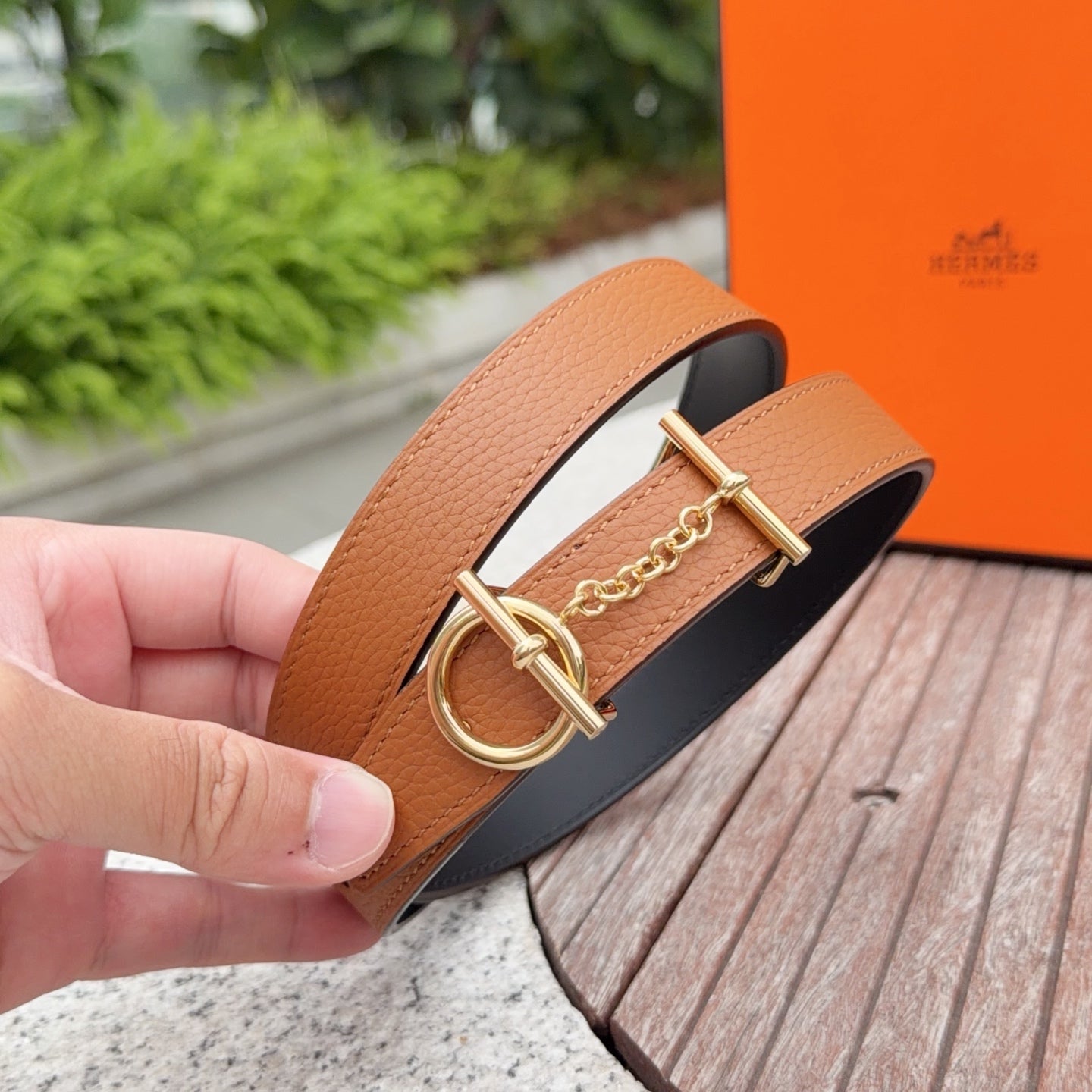 Tan leather belt with round gold buckle and linked chain, held close-up