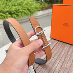 Hermes leather belt held in hand, tan strap with dark back and silver buckle