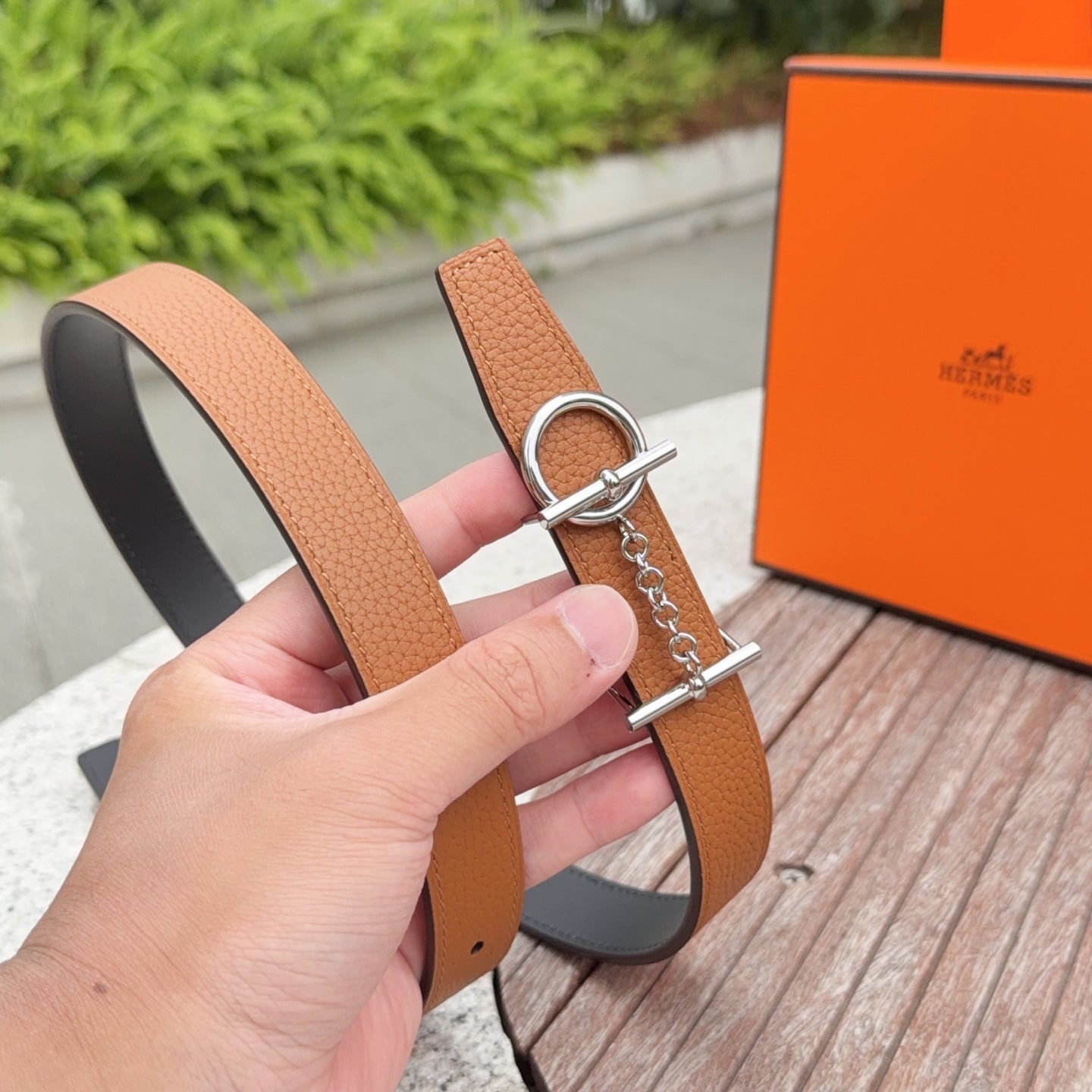 Hermes leather belt held in hand, tan strap with dark back and silver buckle