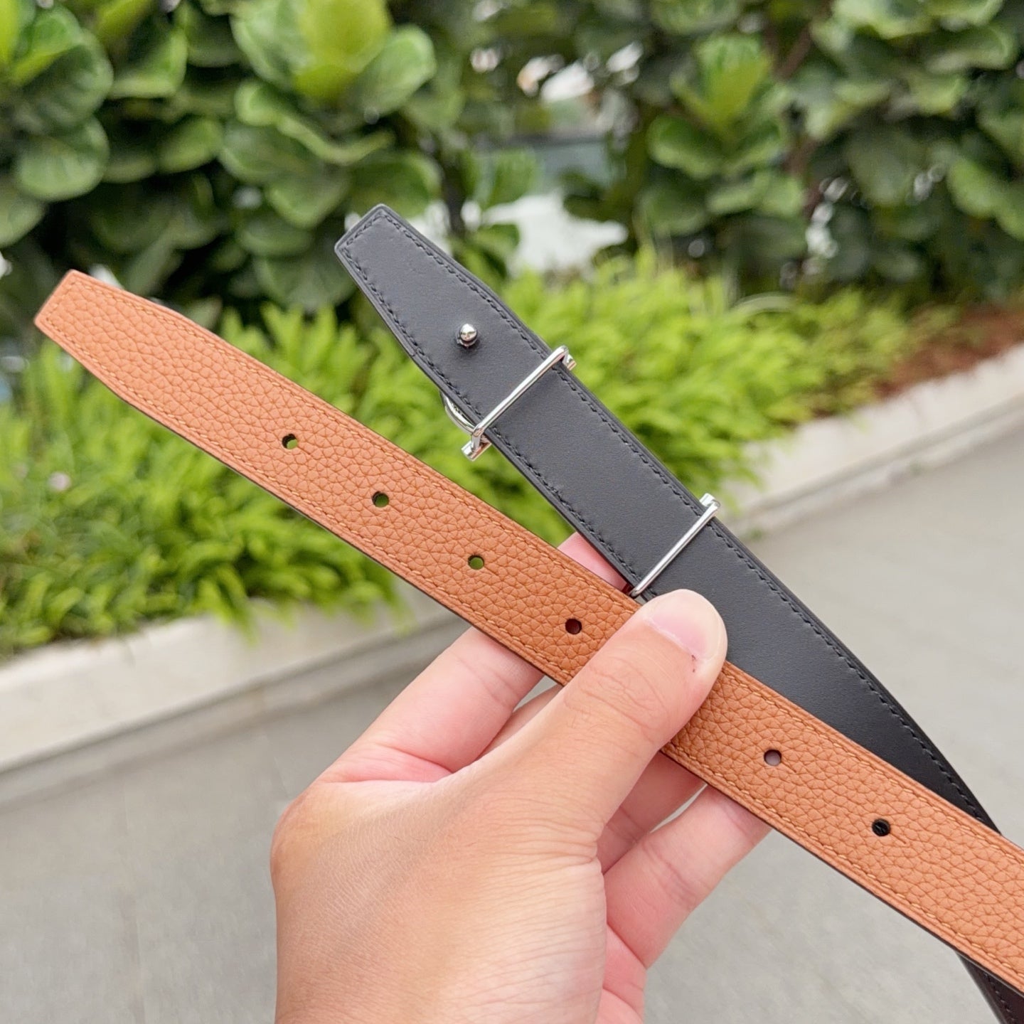 Hermes leather belt close-up with tan and dark straps, silver pin clasp and holes
