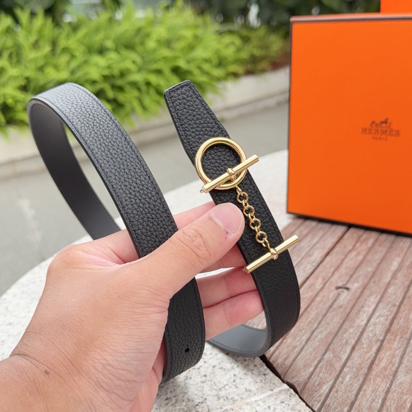 Charcoal leather belt with gold buckle and chain; handheld close-up