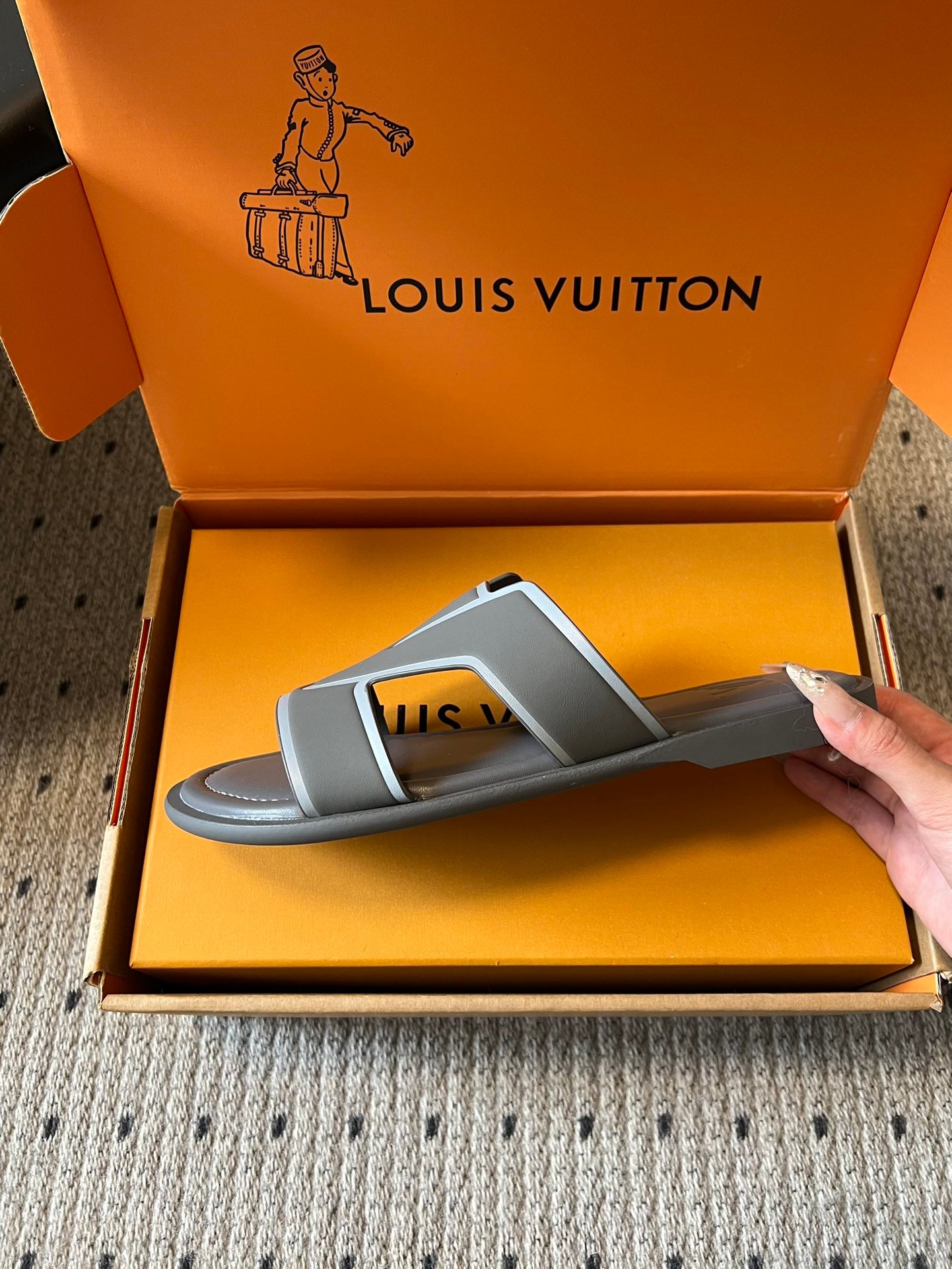 Louis Vuitton slide sandal, dark gray with contrast straps, held over orange box
