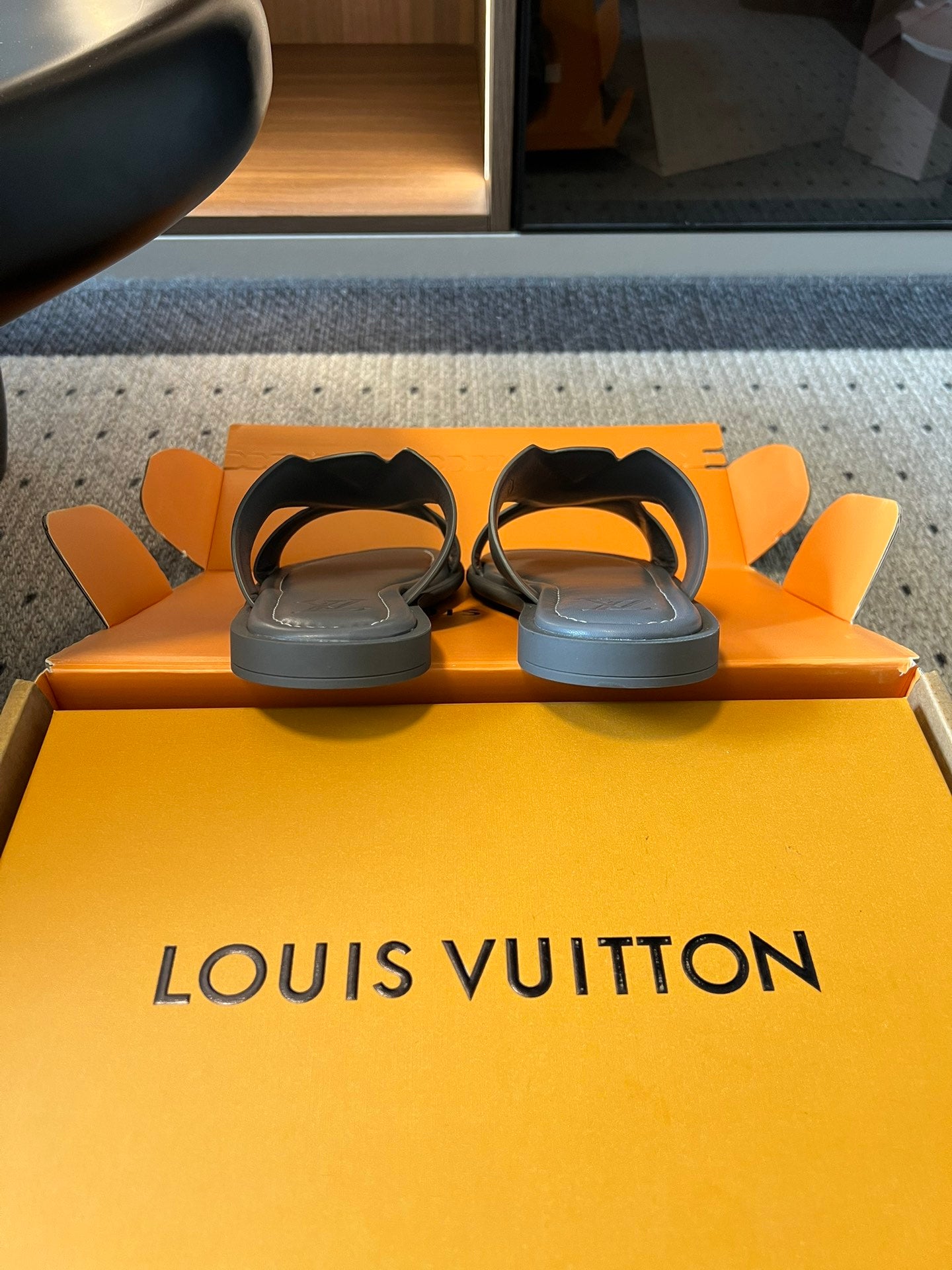 Louis Vuitton slide sandals on orange packaging, dark gray with white V-style straps