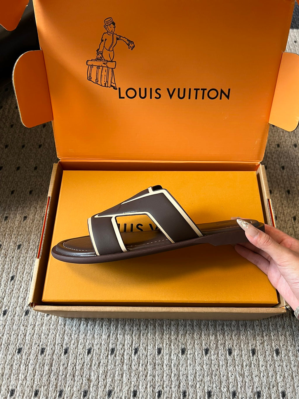 Dark slide sandals with white V strap, held over open shoe box