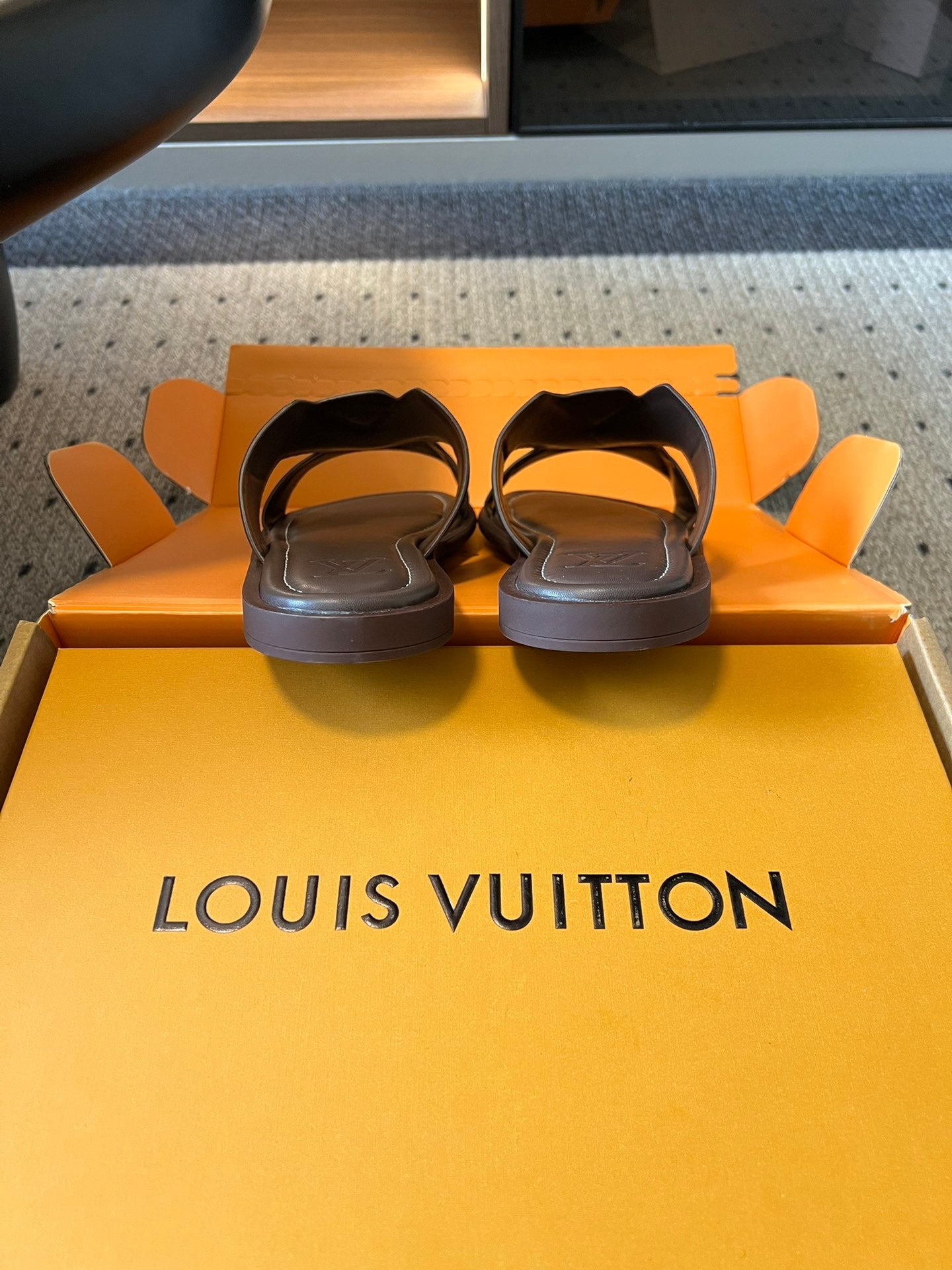 Dark slide sandals with low heel, resting in open shoe box