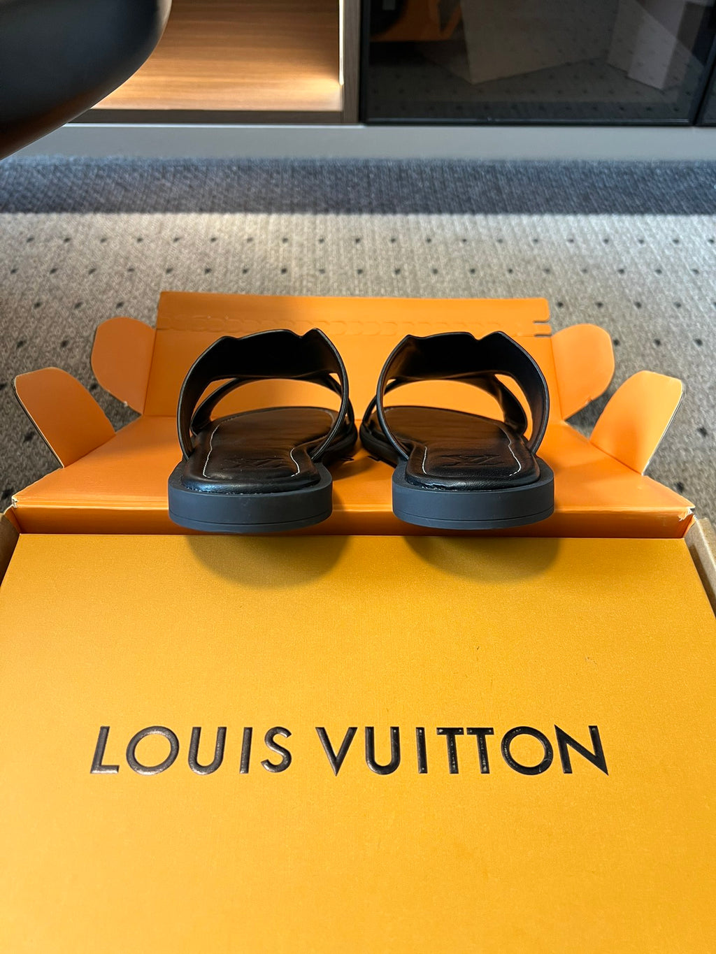 Louis Vuitton sandals on box top, black slides with open toe and low-profile soles