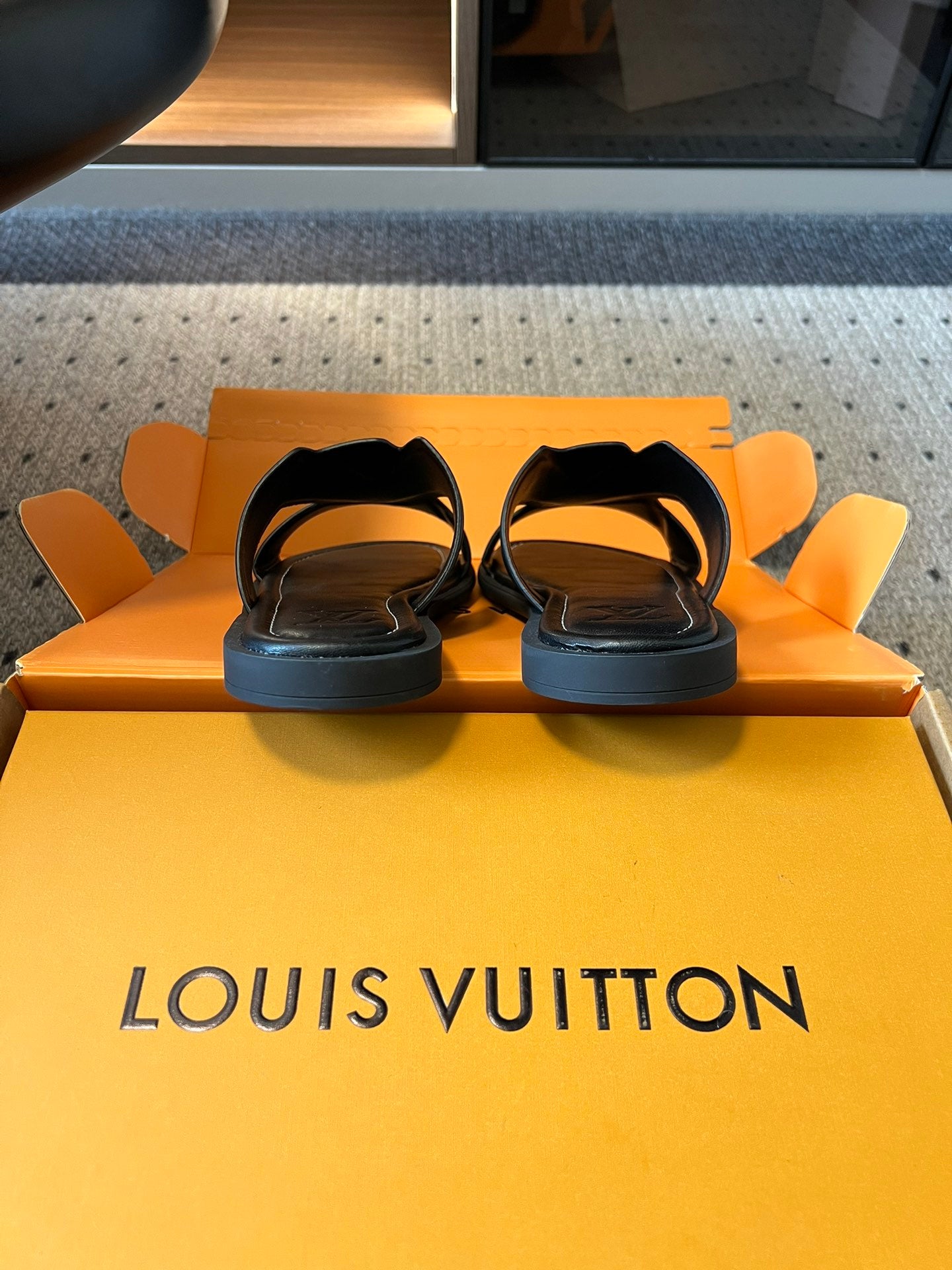 Louis Vuitton sandals on box top, black slides with open toe and low-profile soles