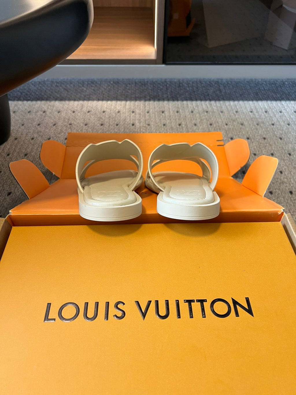 Cream slide sandals resting on Louis Vuitton orange box base, pair view