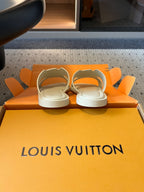 Cream slide sandals resting on Louis Vuitton orange box base, pair view