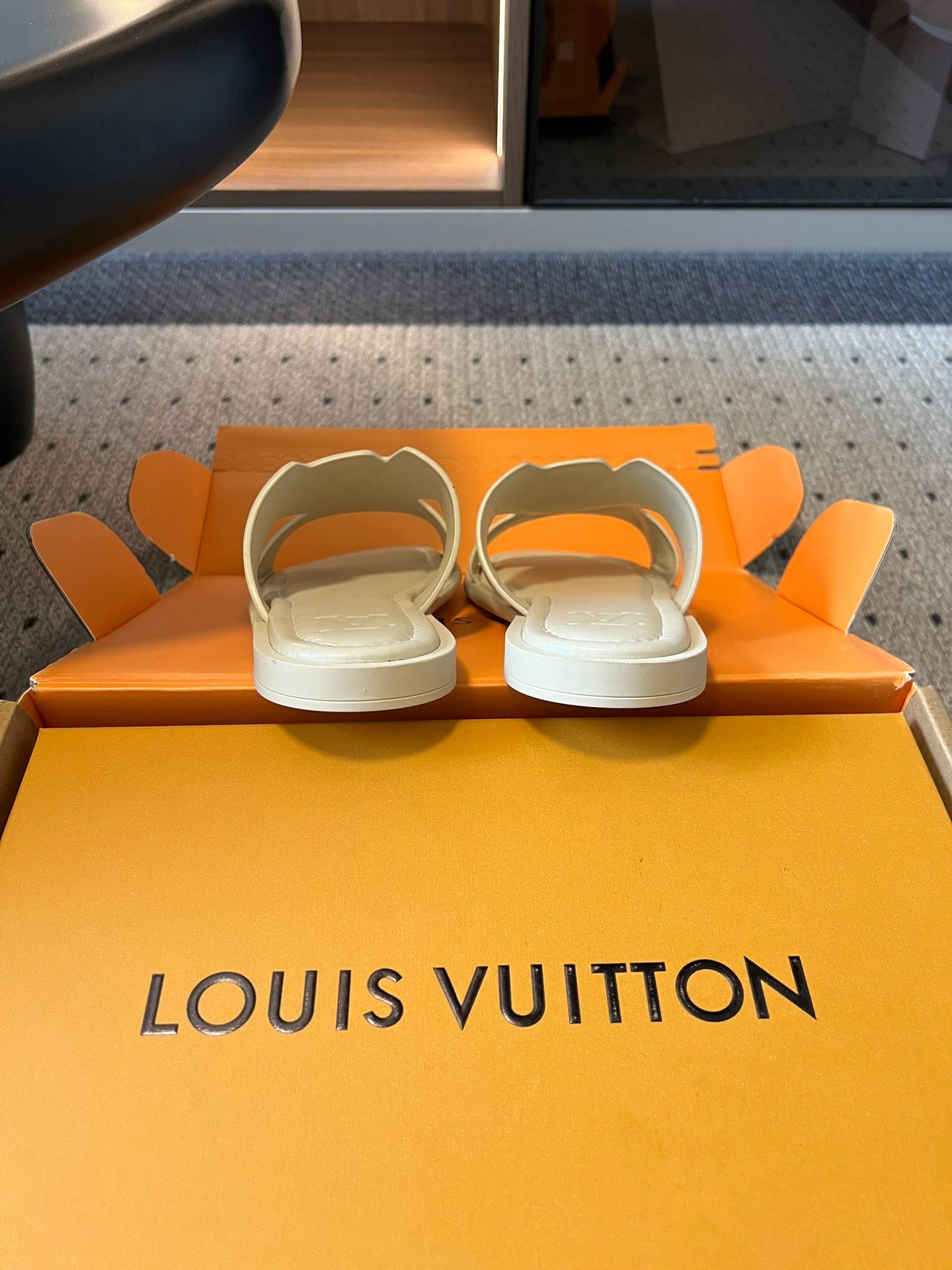 Cream slide sandals resting on Louis Vuitton orange box base, pair view