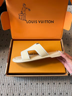 Cream slide sandal held above open box, V-shaped strap and cushioned footbed