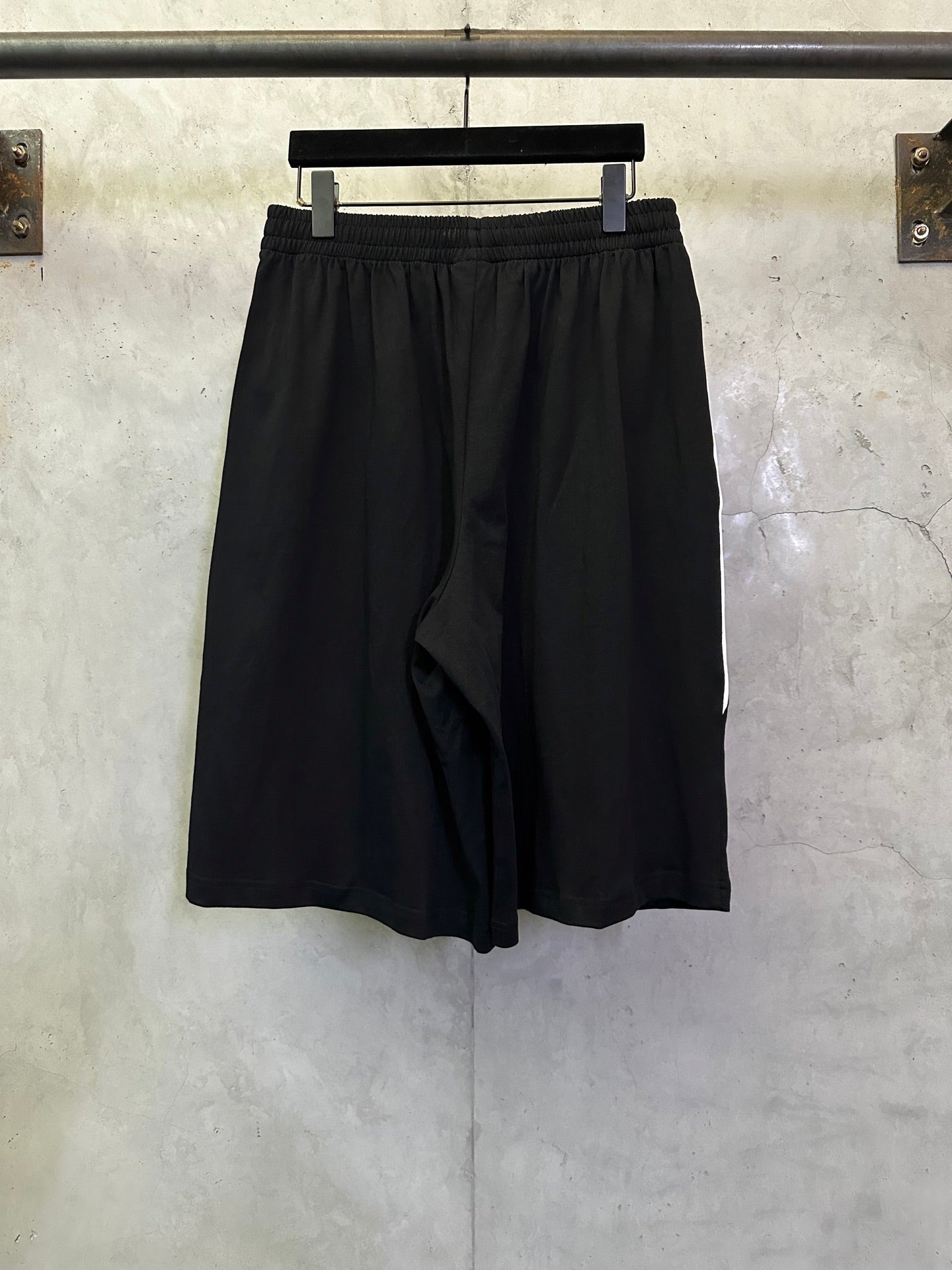 Black shorts front view with elastic waistband and loose draped panel.