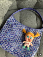 Blue patterned handbag with shoulder handles and plush charm keychain on front.