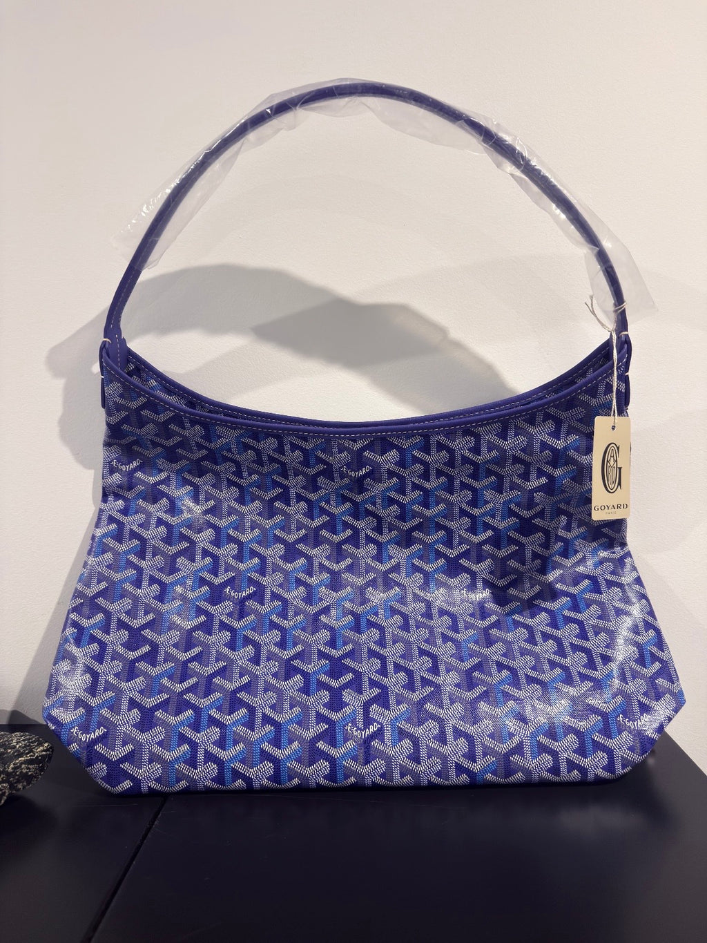 Blue patterned mini bag with top handle and small hanging label on side.