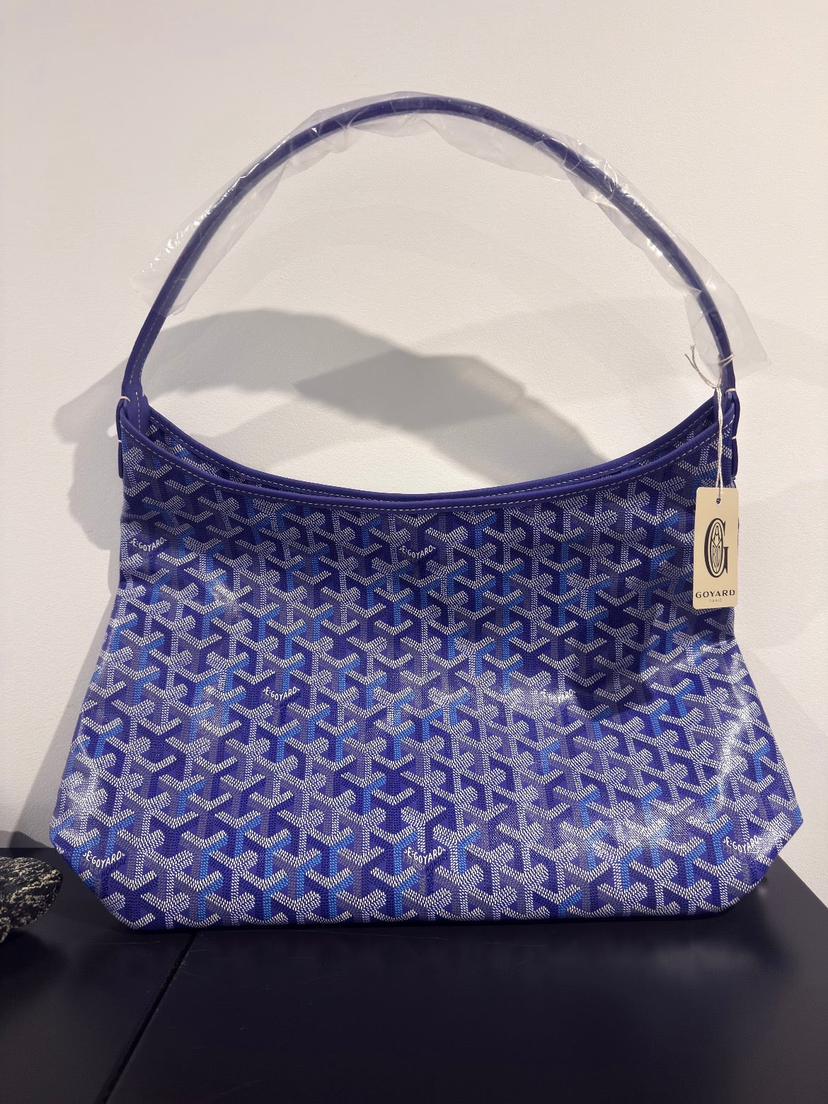 Blue patterned mini bag with top handle and small hanging label on side.