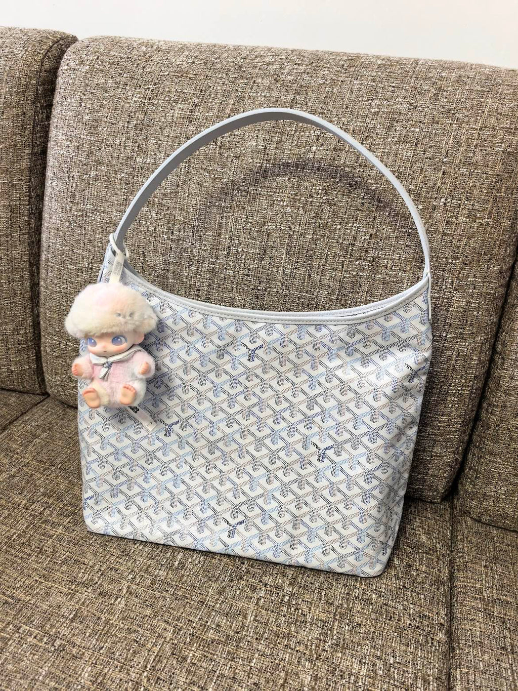 Goyard handbag in light blue with white pattern and plush charm on strap.