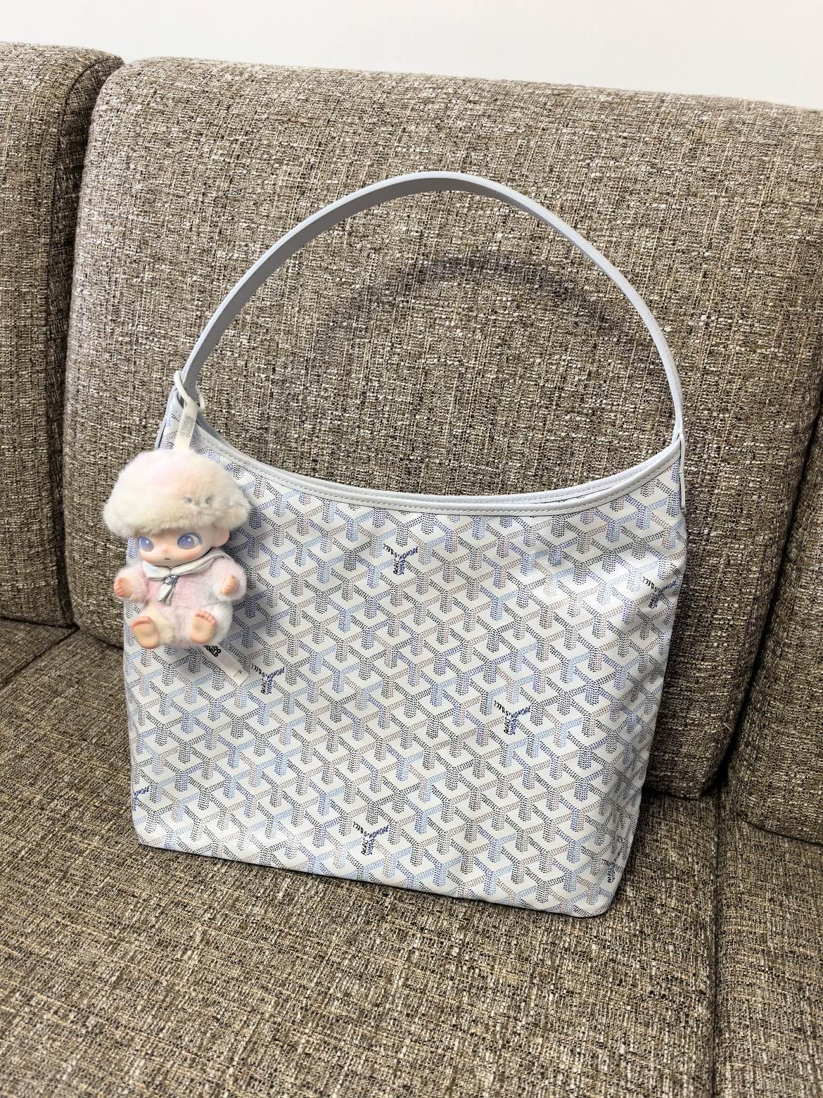 Goyard handbag in light blue with white pattern and plush charm on strap.