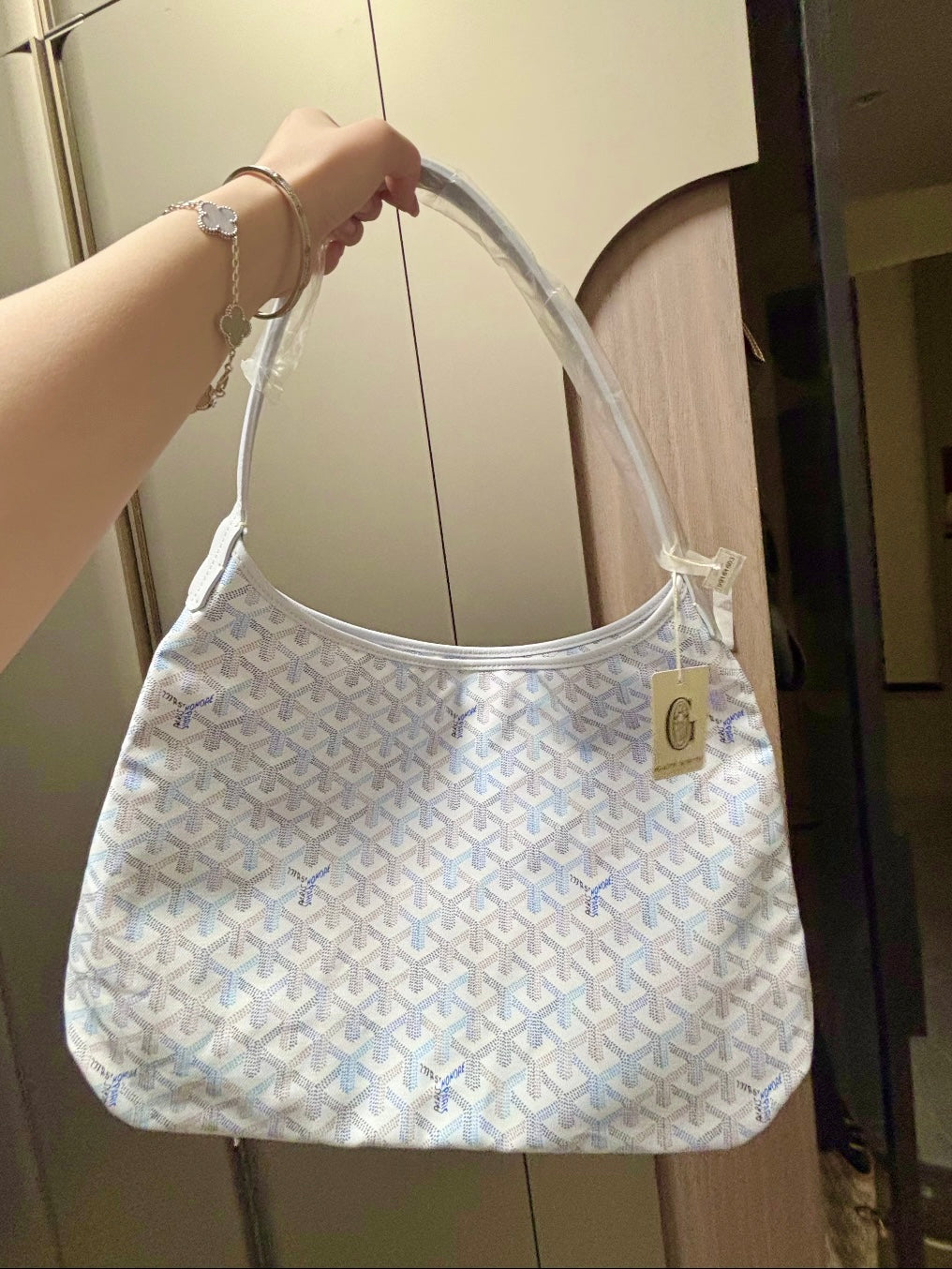 Goyard handbag in light blue with white pattern, shown on hand, side tag detail.