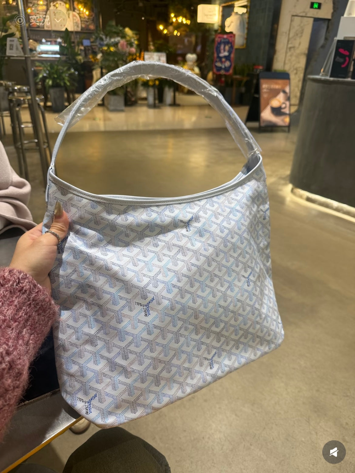 Goyard handbag in light blue with white pattern, held by hand with open top.