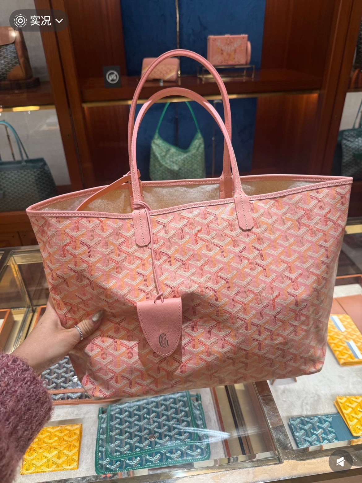 Pink patterned tote bag with top handles, detachable charm, and front pouch detail, front view.