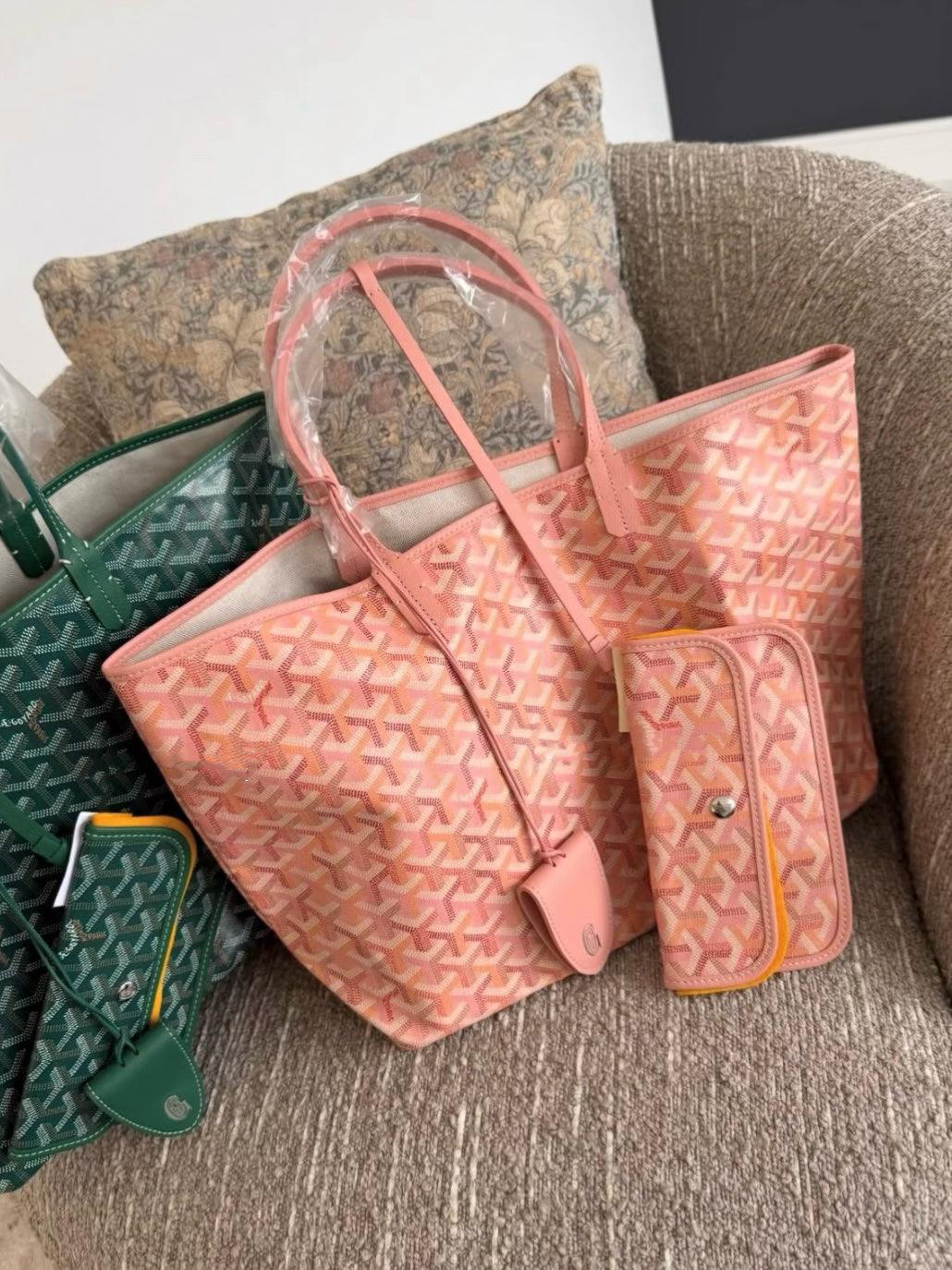 Pink patterned tote bag with matching small pouch and wrist strap, sofa side view.