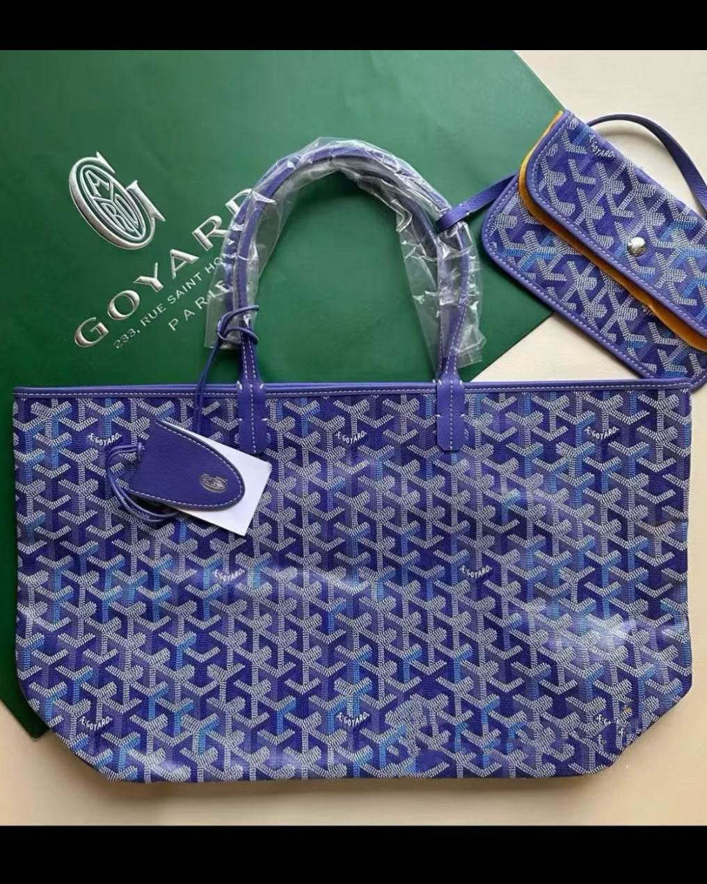 Blue patterned tote bag with top handles, front leather logo patch, and hanging charm