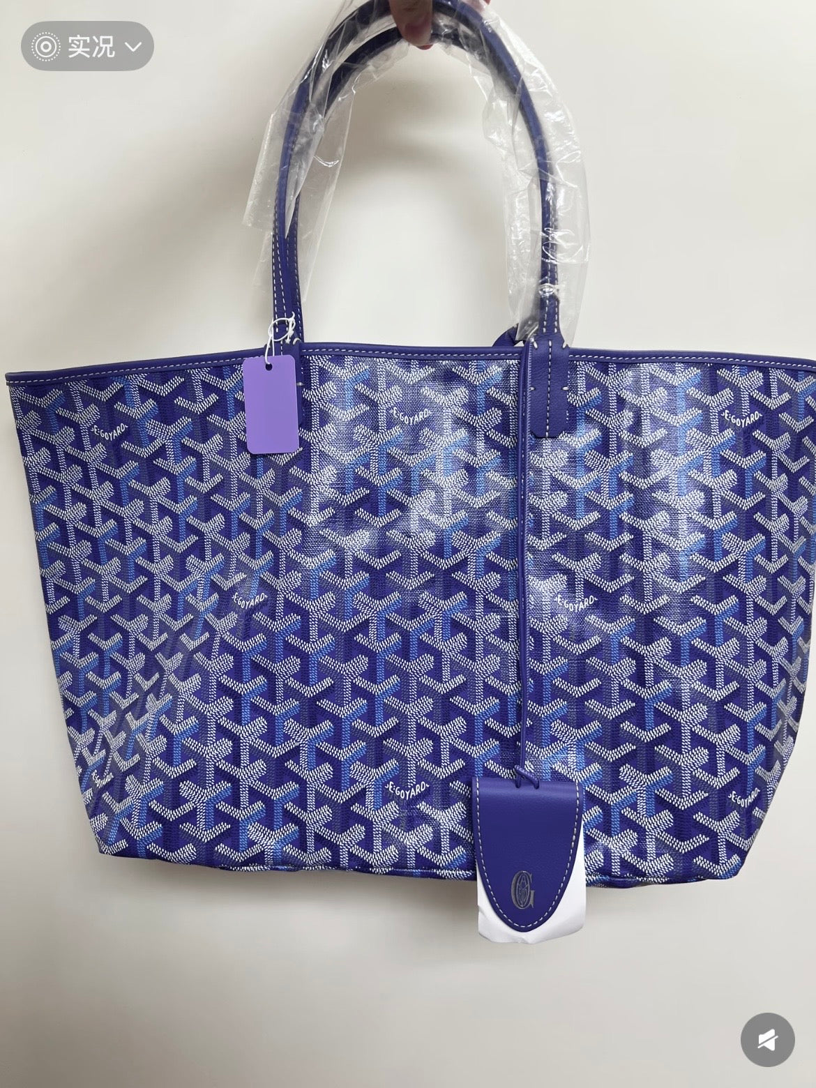Blue patterned tote bag with top handles and leather logo patch, side view