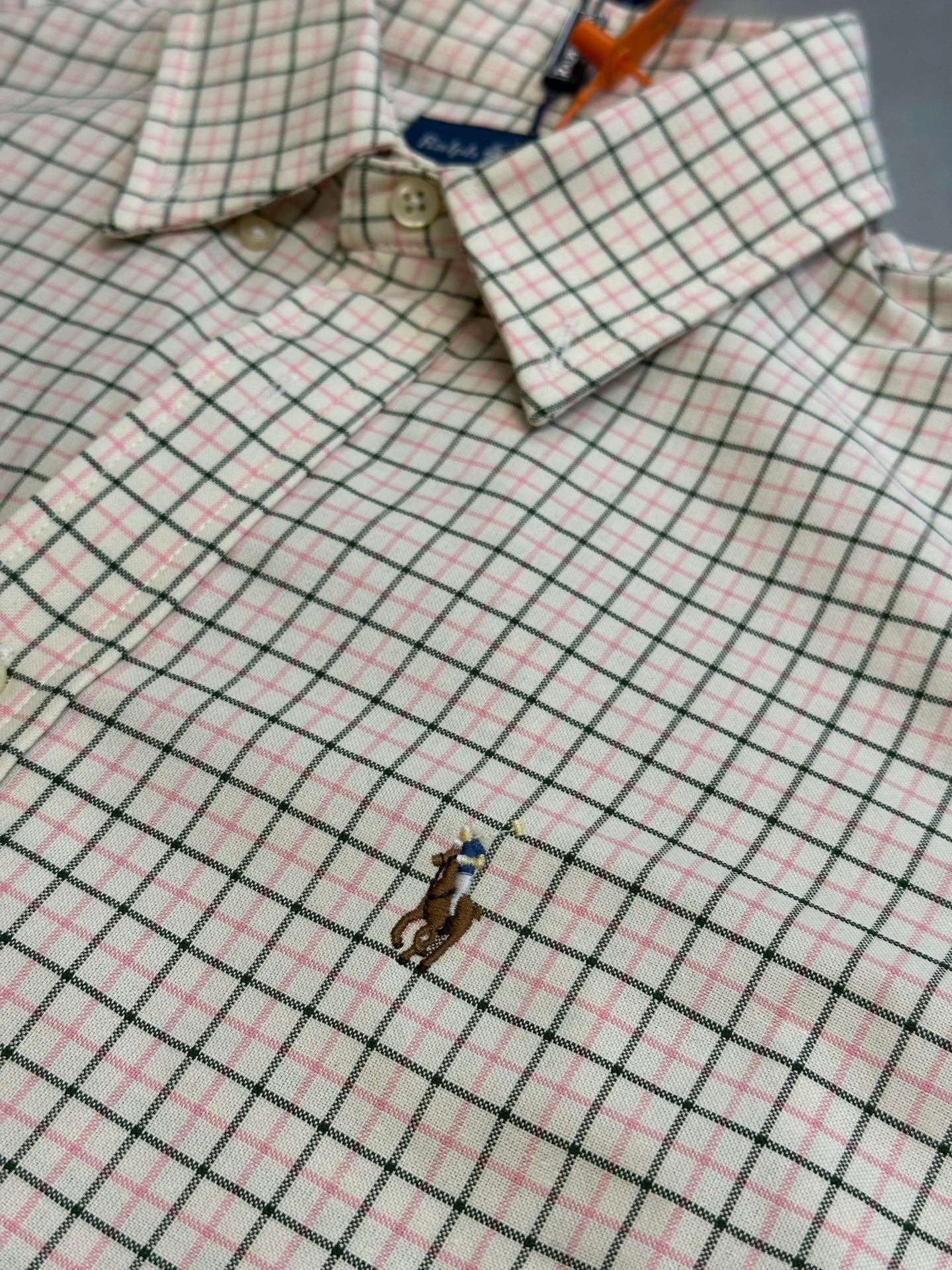 Plaid shirt close-up showing embroidered logo and buttoned cuffs.