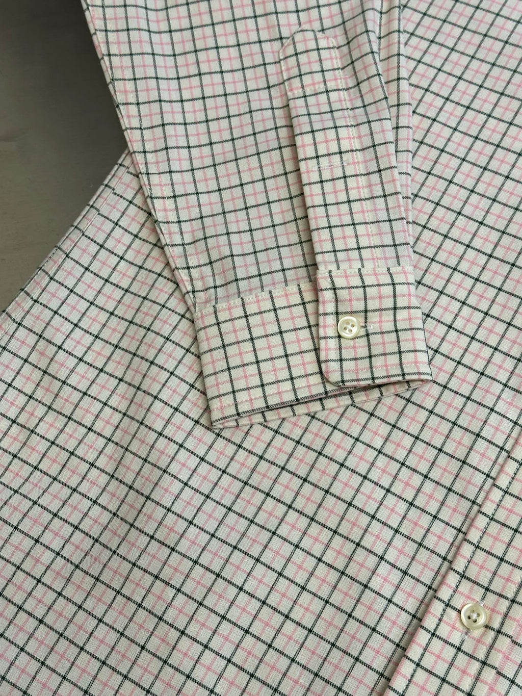 Plaid shirt cuff and hem close-up with button detail and stitching.