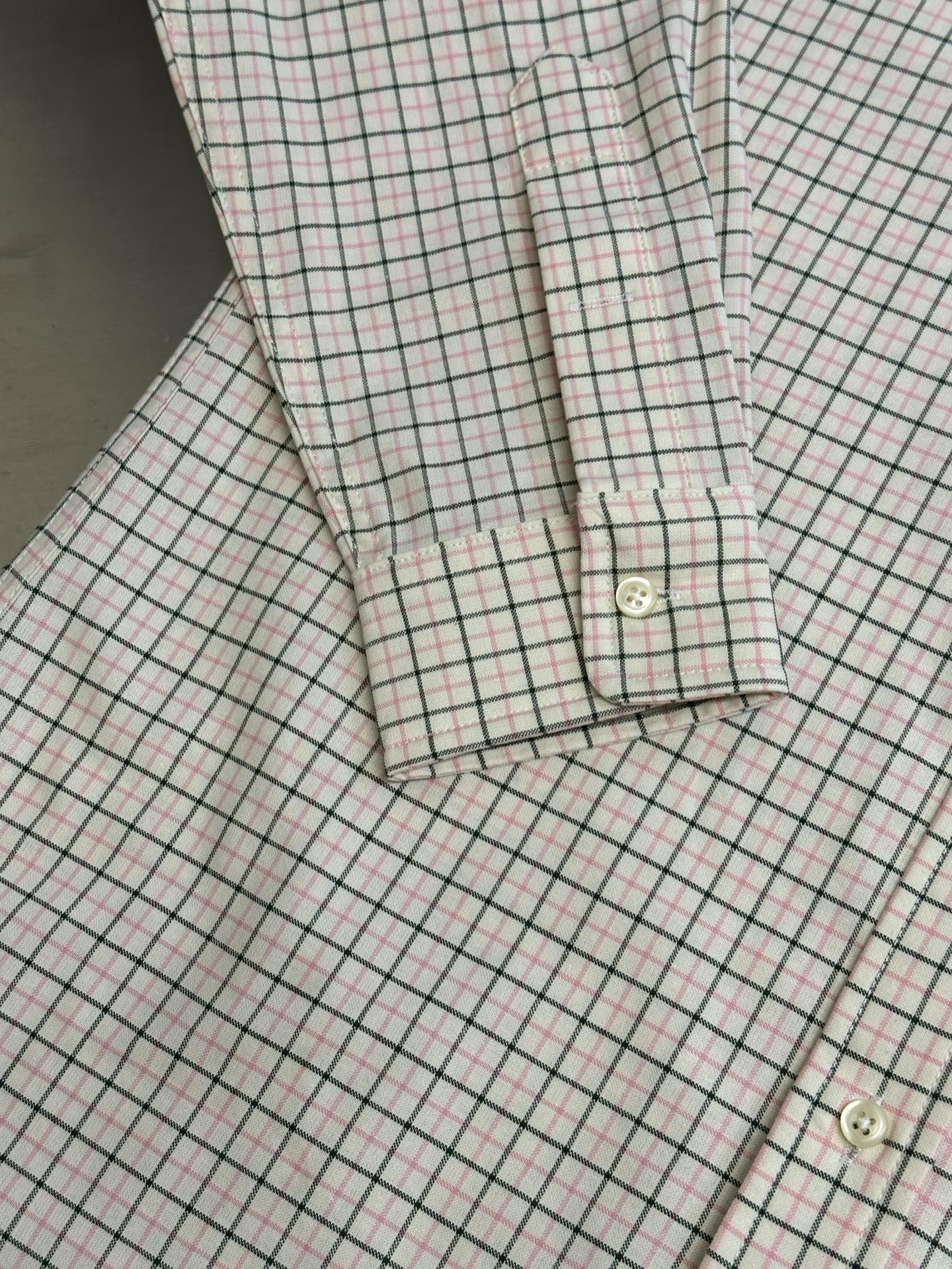 Plaid shirt cuff and hem close-up with button detail and stitching.