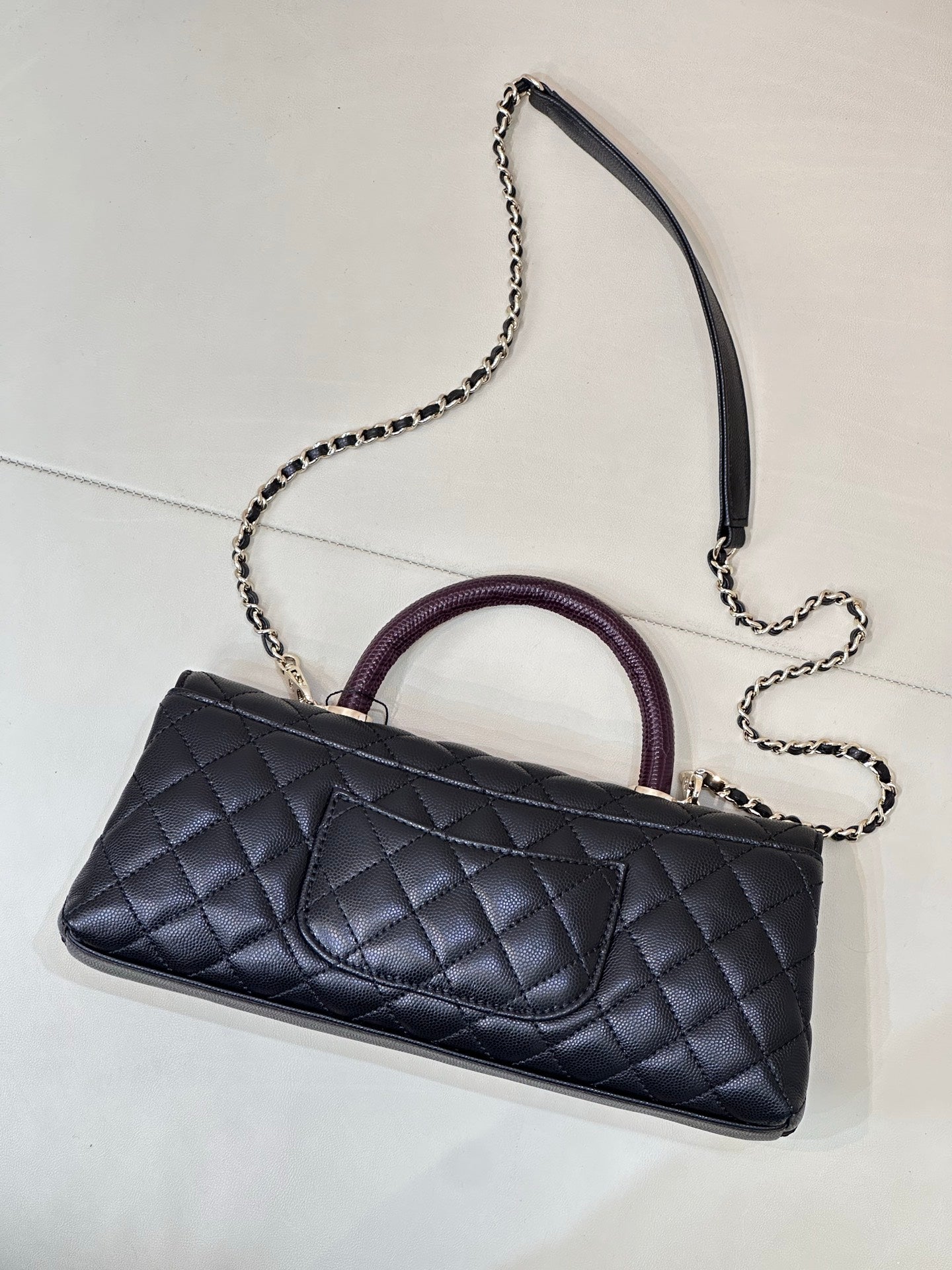 Chanel bag side view with dark navy quilted leather, purple handle, and chain strap