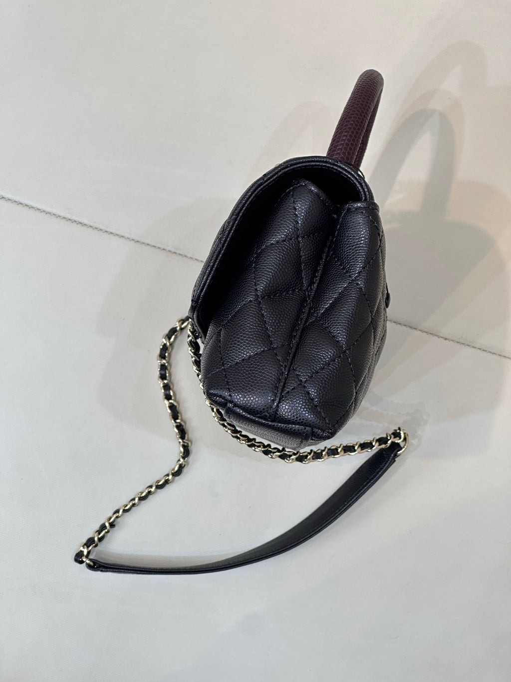 Chanel bag side view in dark navy quilted leather with purple top handle and chain