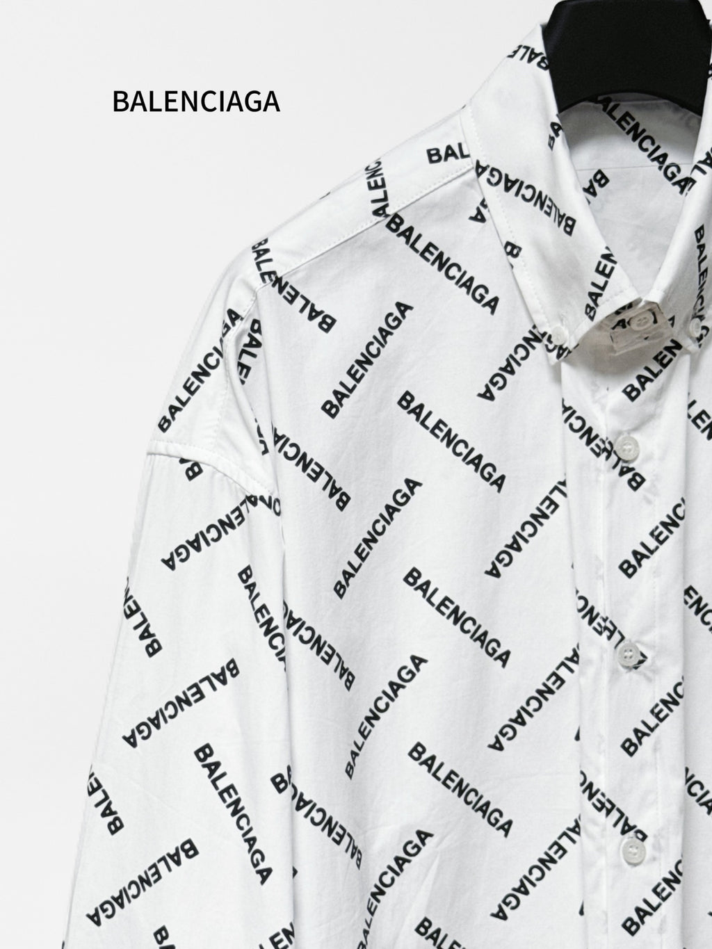 White long-sleeve button-up shirt with black Balenciaga logo pattern, angled close-up