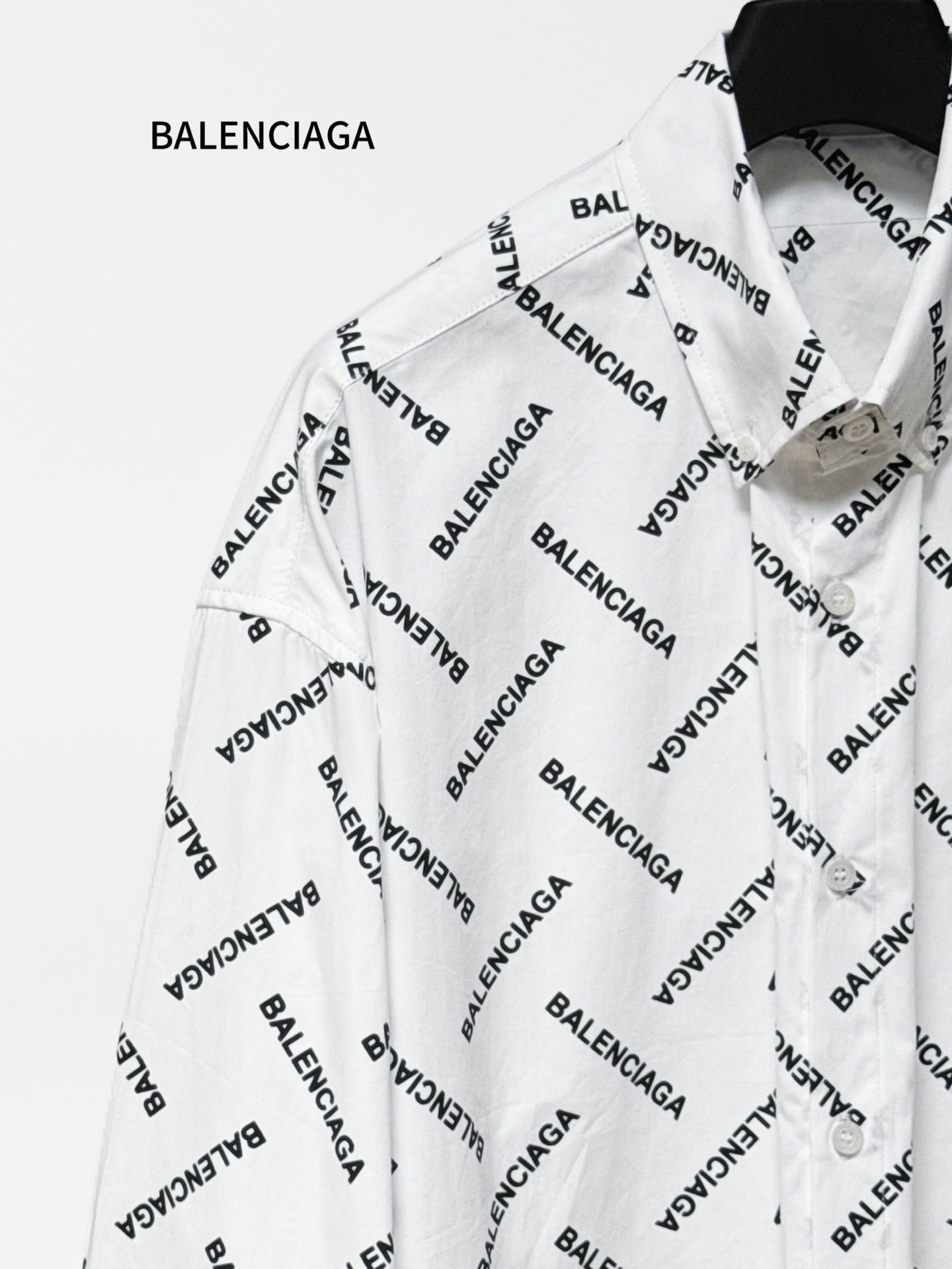 White long-sleeve button-up shirt with black Balenciaga logo pattern, angled close-up