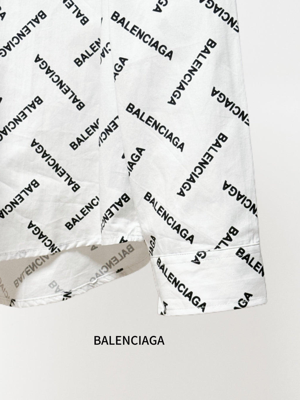White long-sleeve button-up shirt hem with black Balenciaga logo print detail