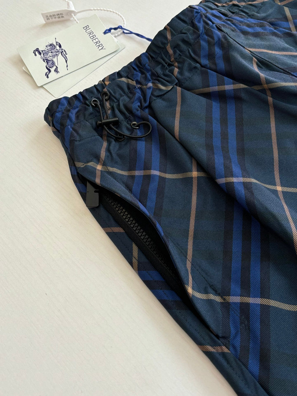 Navy plaid shorts fabric close-up with elastic waistband and drawcord ties