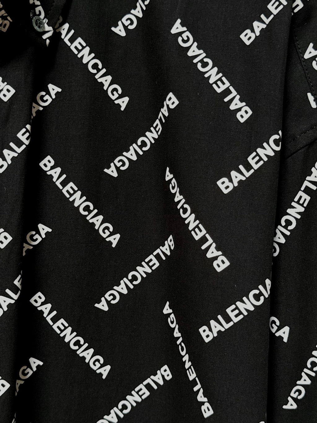 Black fabric close-up with Balenciaga logo print and visible button-front placket