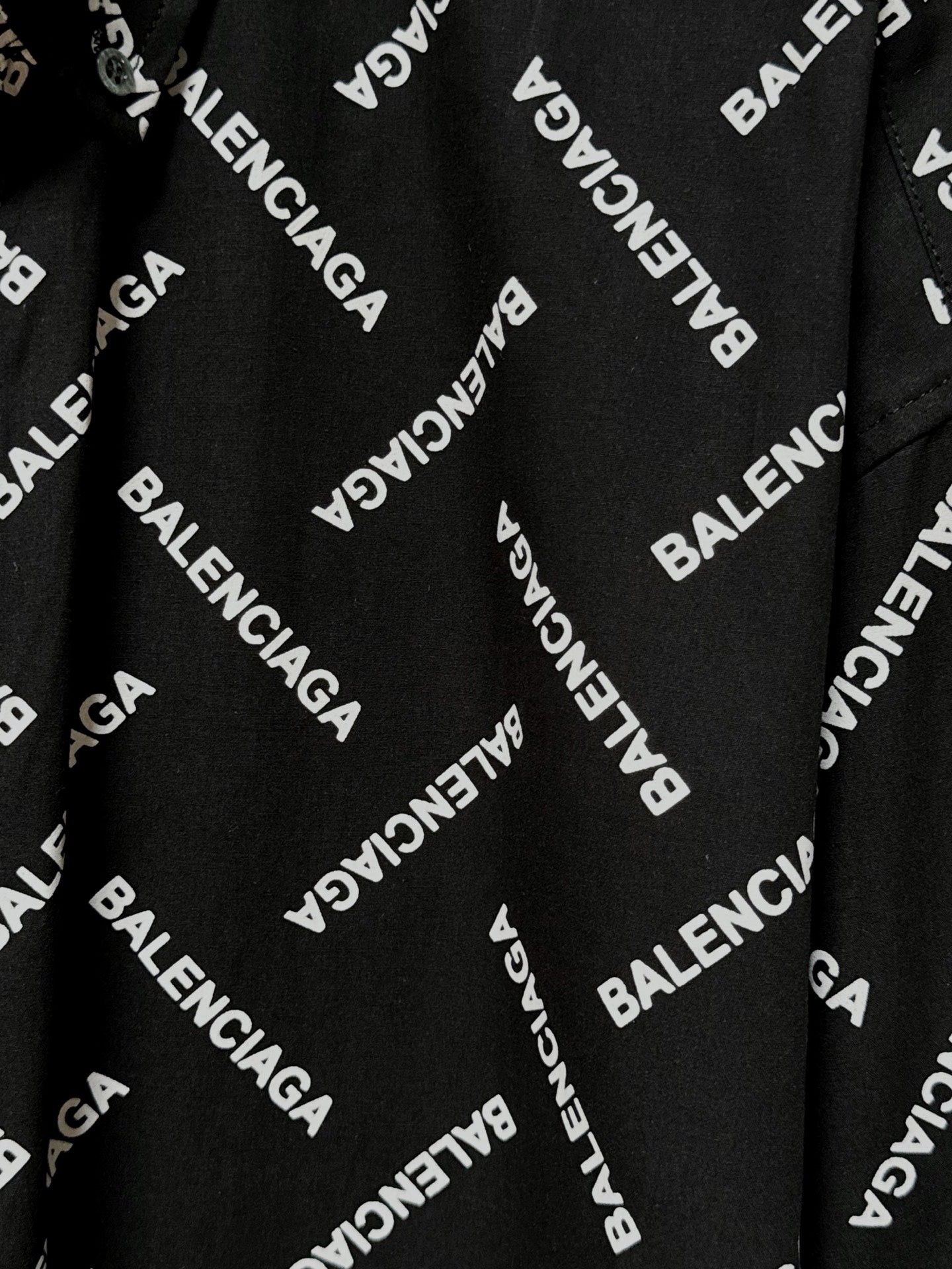 Black fabric close-up with Balenciaga logo print and visible button-front placket