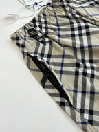 Plaid pants fabric close-up with black drawstring and zipper, beige with blue and black checks