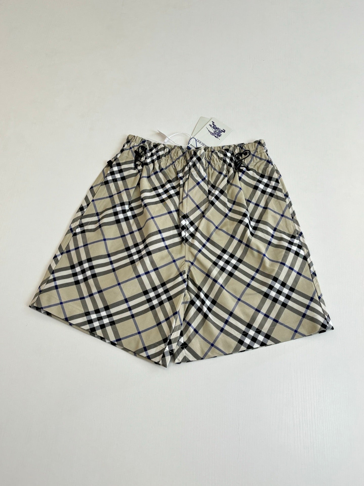 Plaid pants laid flat, gathered elastic waistband with drawstring, beige blue and black checks