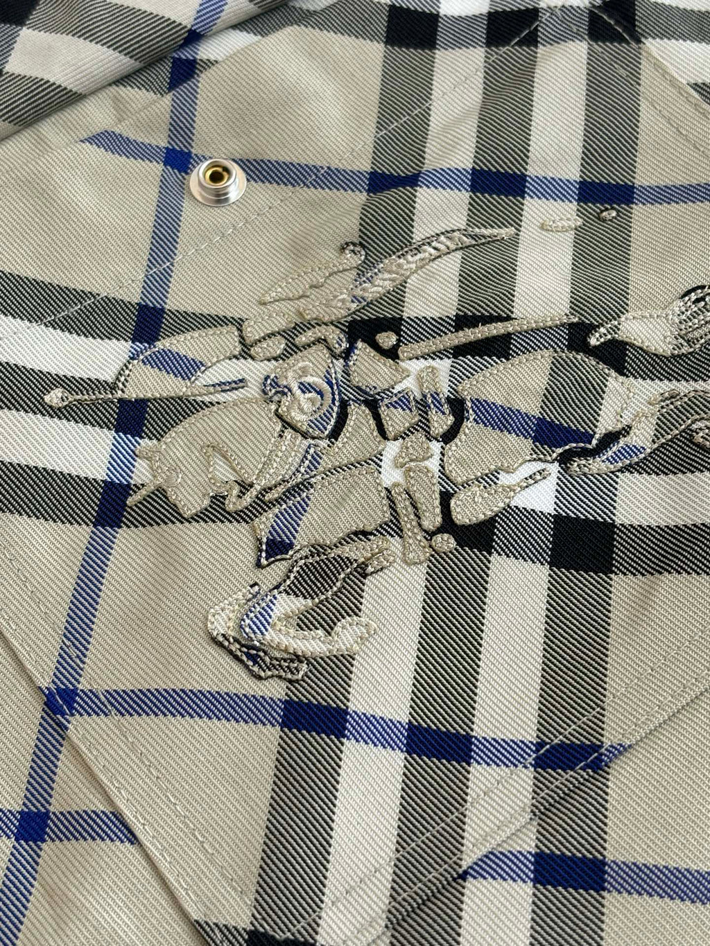 Embroidered emblem on plaid pocket, beige blue and black checks with metal eyelet detail