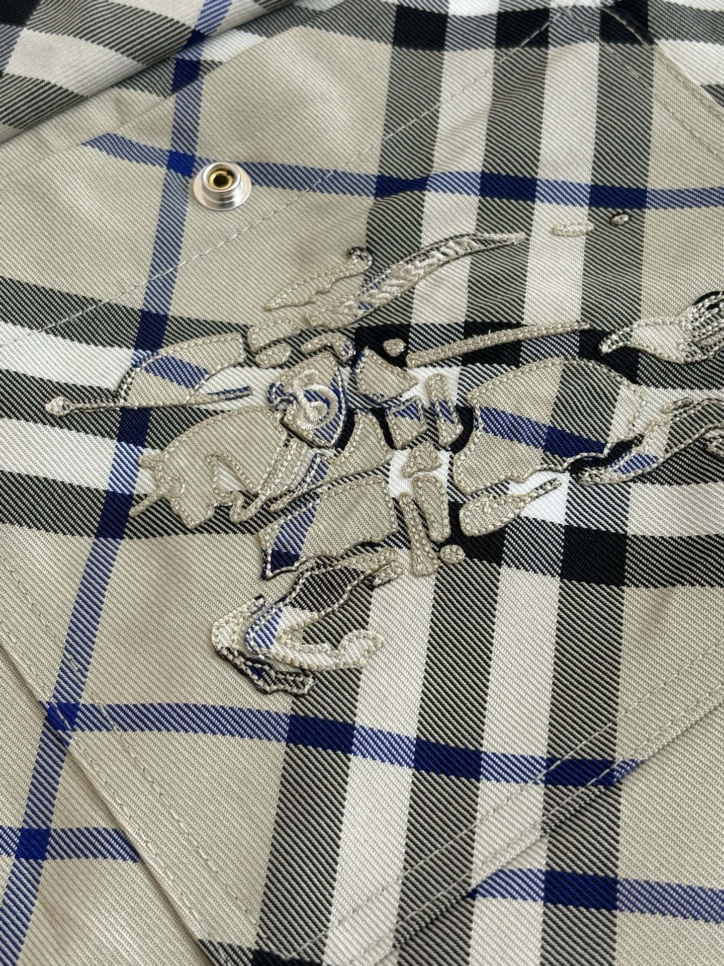 Embroidered emblem on plaid pocket, beige blue and black checks with metal eyelet detail