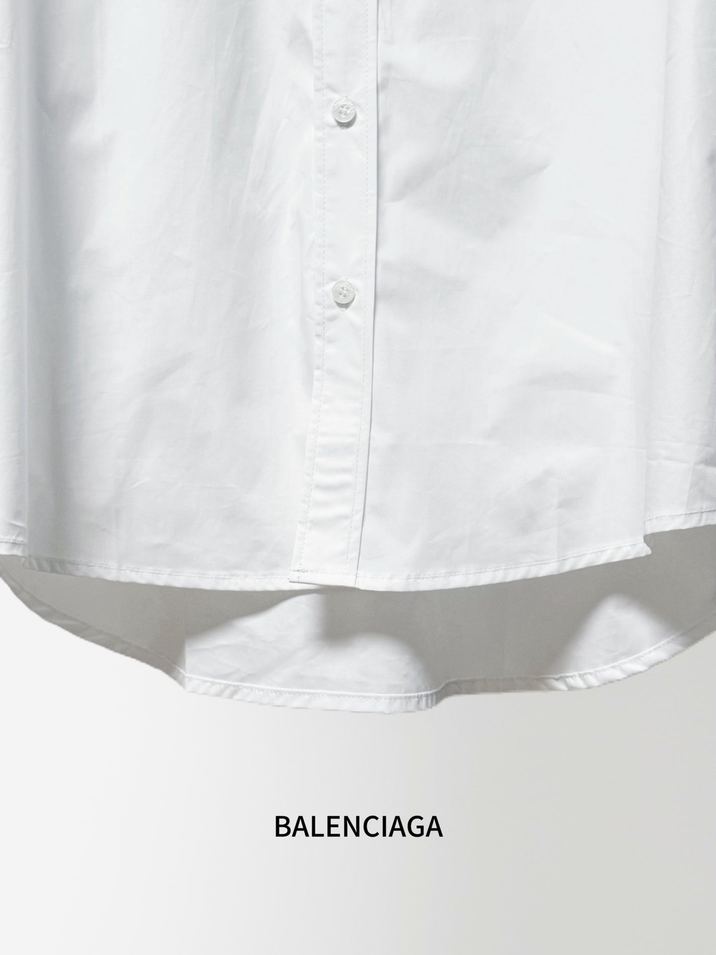 White long-sleeve button-up shirt hem with buttons and gathered fabric at waist