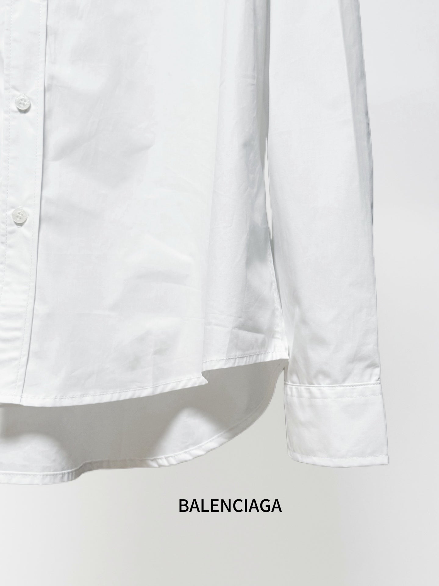 White long-sleeve button-up shirt lower side with curved hem and cuff edge