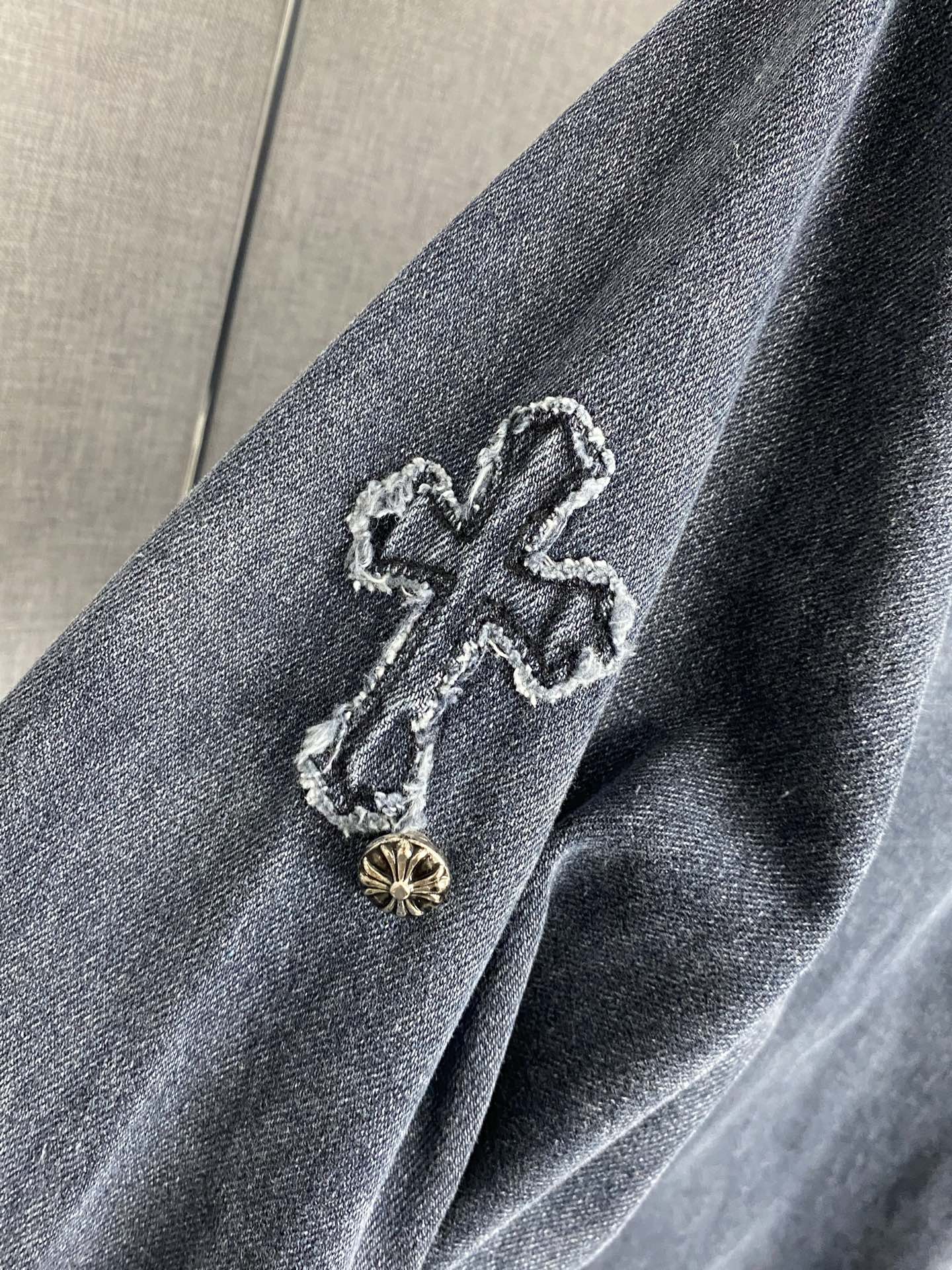 Denim jacket shoulder with embroidered cross patch and gold-toned button