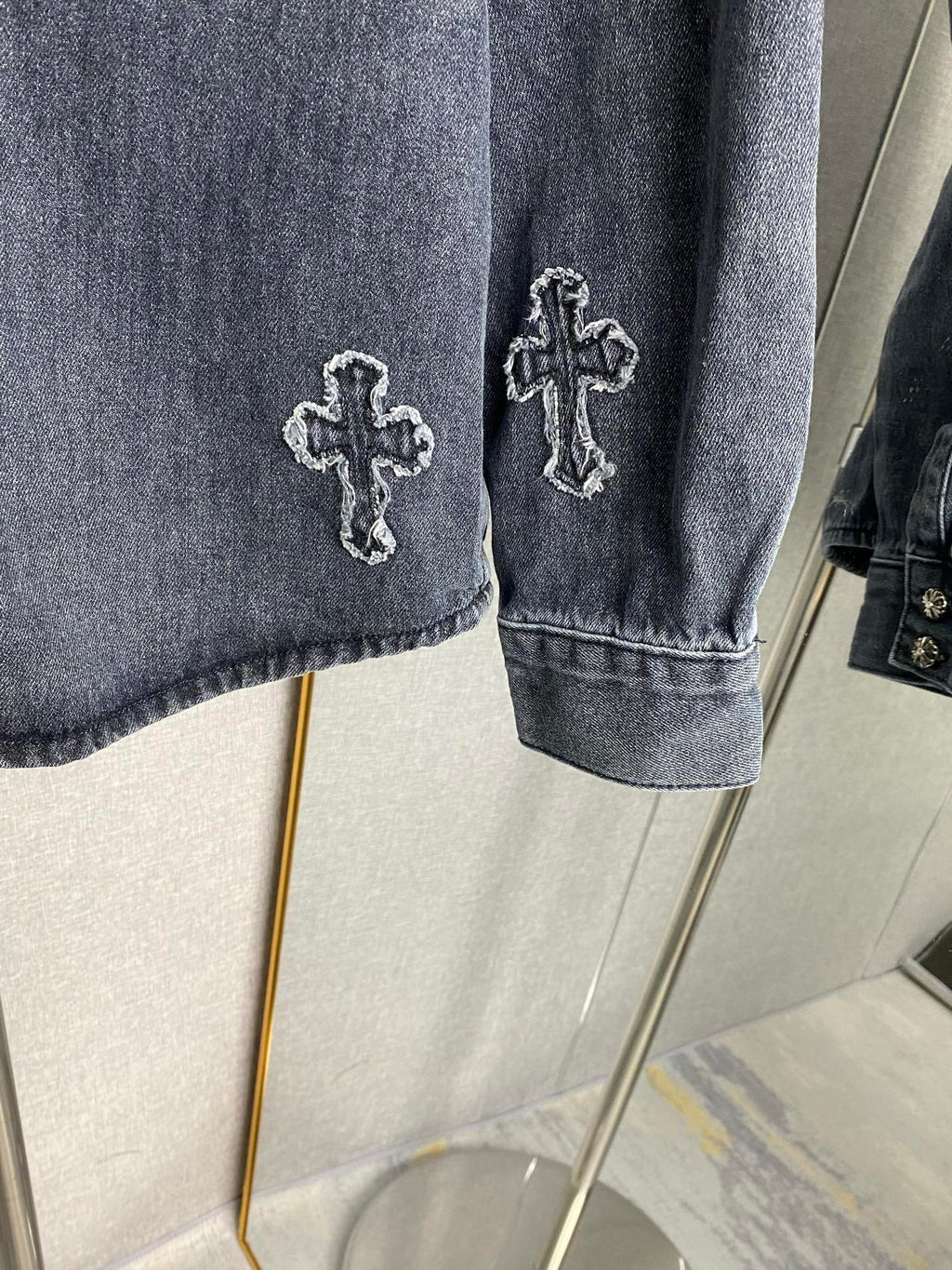 Denim jacket sleeve with embroidered cross patch and buttoned cuff