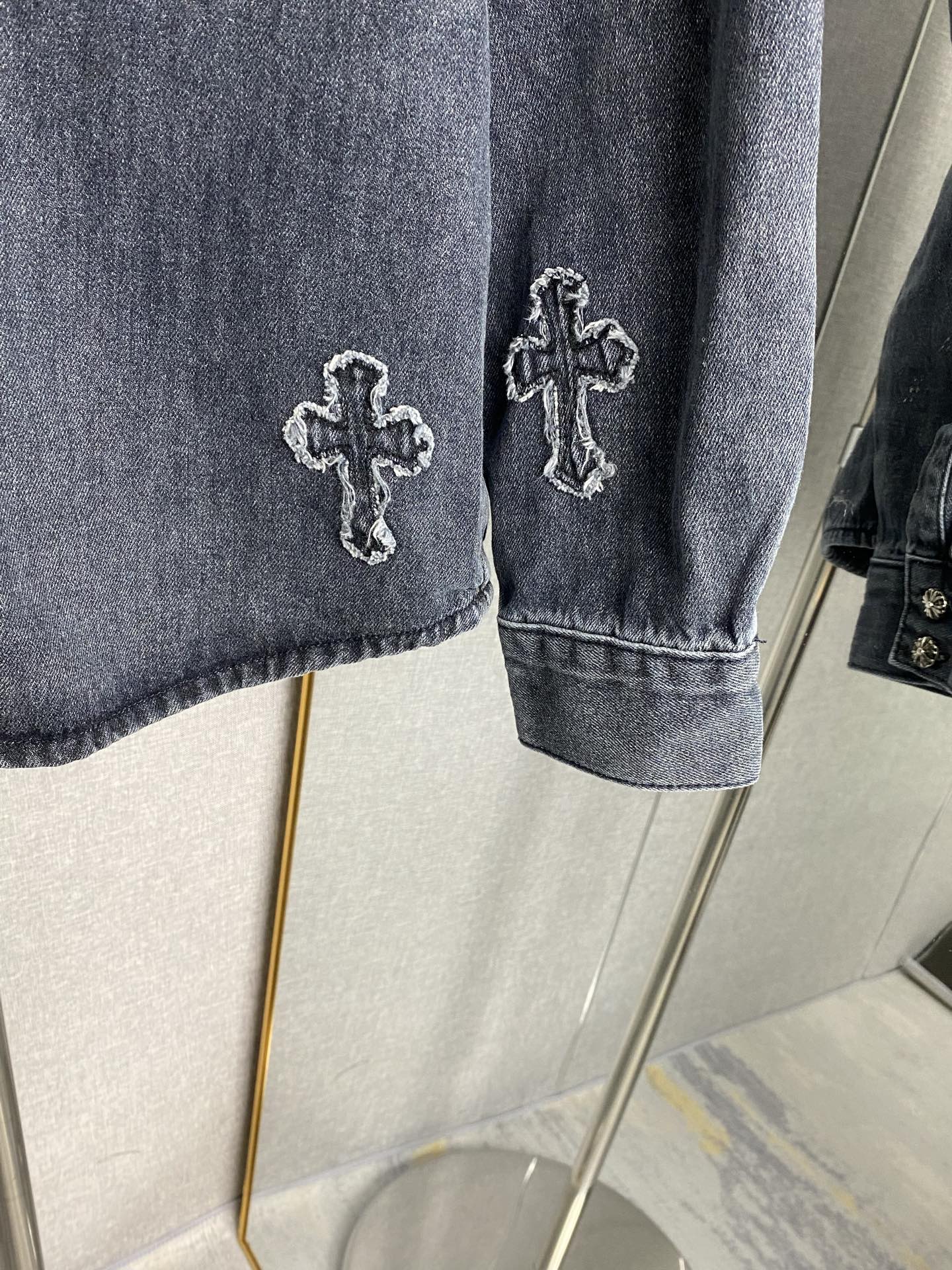 Denim jacket sleeve with embroidered cross patch and buttoned cuff