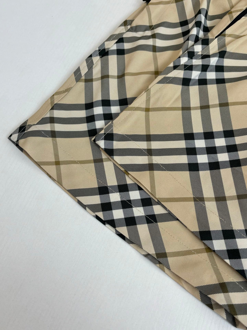 Burberry plaid shorts fabric close-up, intersecting beige and black check lines.