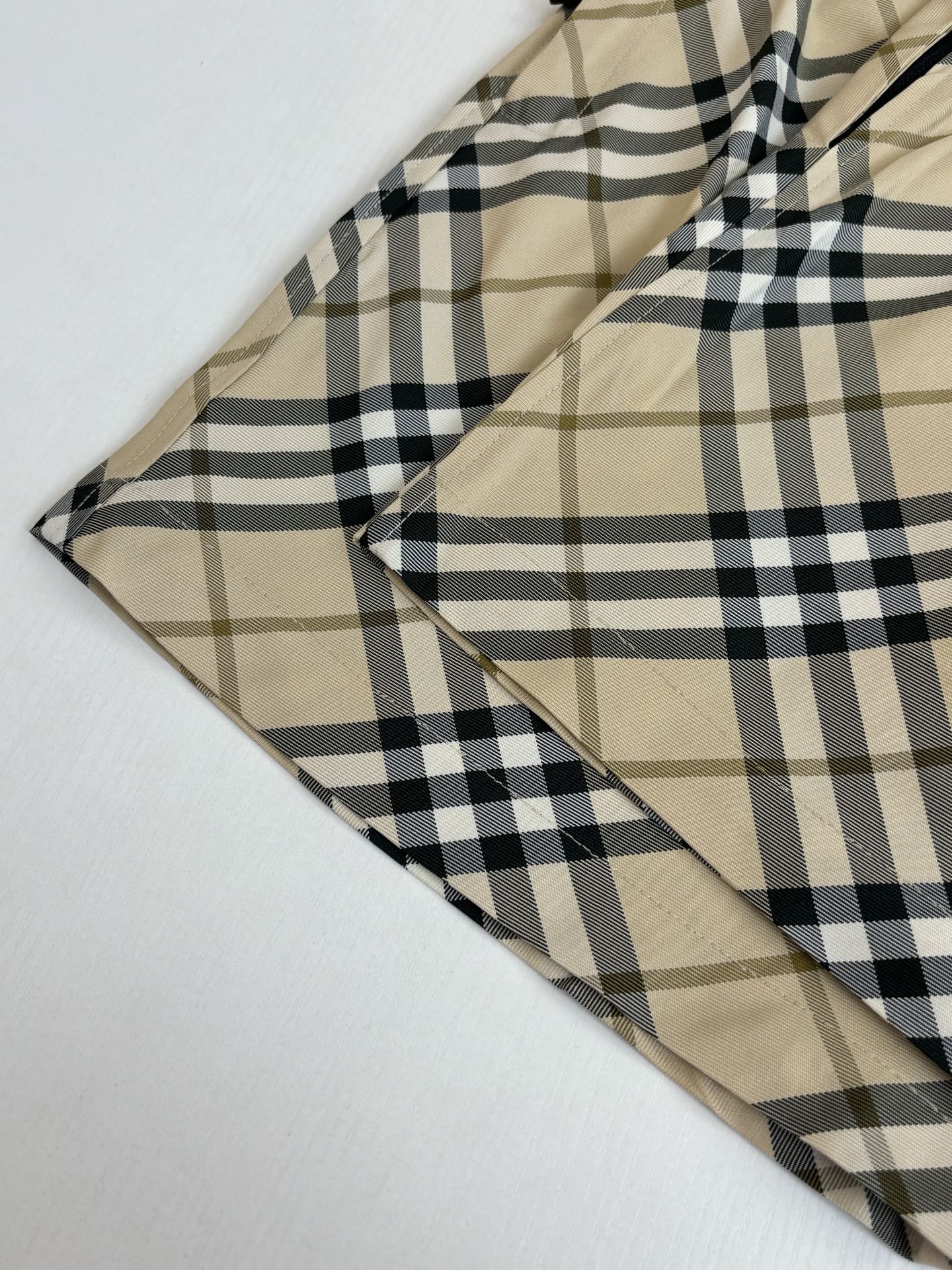 Burberry plaid shorts fabric close-up, intersecting beige and black check lines.